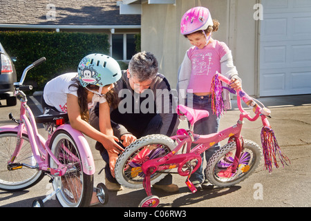 Dad and big sister adjust the training wheels of his five year old daughter's bicycle as she learns to ride in California. Stock Photo