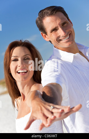 Attractive middle aged man and woman romantic couple in white clothes holding hands to camera on a tropical beach Stock Photo