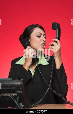 Businesswoman using multiple landline phones and shouting Stock Photo