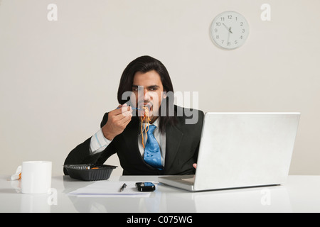Businessman eating noodles while using a laptop at the desk Stock Photo