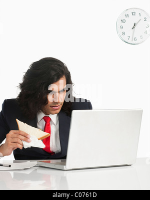 Businessman eating a sandwich while using a laptop at the desk Stock Photo