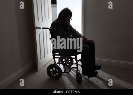 Man in wheelchair, sitting alone in a dark room. Stock Photo