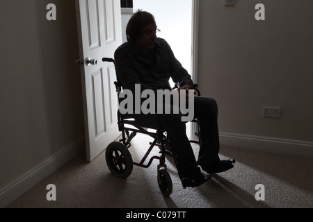 Man in wheelchair, sitting alone in a dark room. Stock Photo