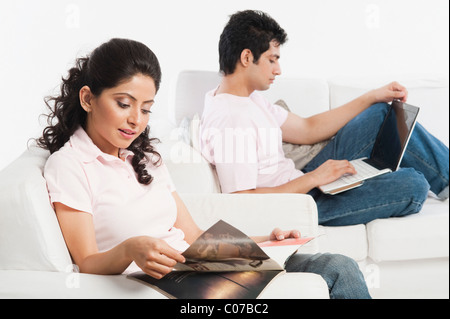 Woman reading a magazine with a man using a laptop Stock Photo