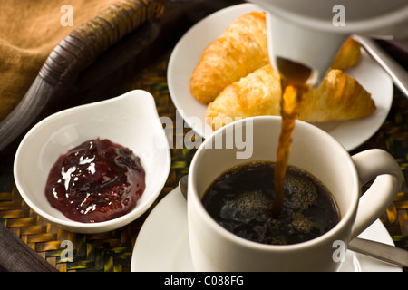 A tray with croissants, jam and a cup of hot black coffee being poured Stock Photo