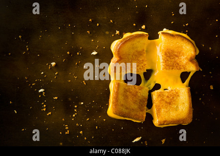 A Grilled Cheese Sandwich cut in four squares pulling the cheese on a wood table Stock Photo