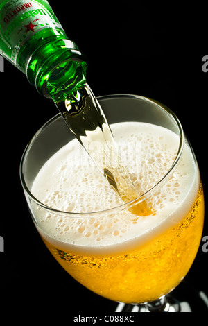 A Bottle of Heineken Beer pouring into a glass on a black background. Stock Photo