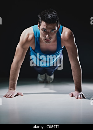 Young caucasian male in sportswear doing push ups on black background. Vertical shape, front view, copy space Stock Photo