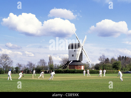 Iconic quintessential England idyllic village green cricket match bowler batsman & fielders Mountnessing Post Mill beyond in Essex countryside UK Stock Photo