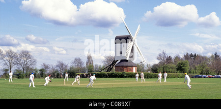 Iconic quintessential England idyllic village green cricket match bowler batsman & fielders Mountnessing Post Mill beyond in Essex countryside UK Stock Photo