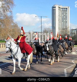 Soldiers & horses of The Blues & Royals mounted regiment Household Cavalry in winter cloaks riding in Hyde Park Hilton Hotel beyond London England UK Stock Photo