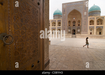 The Mir-i-arab Madrassah seen beyond the ornate carved doors of the Kalon Mosque, Bukhara, Uzbekistan Stock Photo