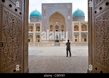 The Mir-i-arab Madrassah seen beyond the ornate carved doors of the Kalon Mosque, Bukhara, Uzbekistan Stock Photo