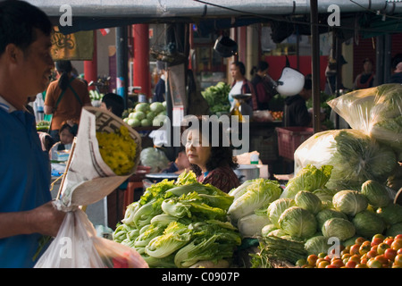 A woman food vendor is sitting near piles of lettuce and tomatoes at an outdoor street food market in Mae Hong Son, Thailand. Stock Photo