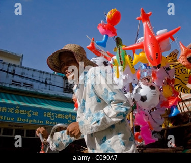A toy balloon salesman wearing a straw hat is working on a city street in Phnom Penh, Cambodia. Stock Photo