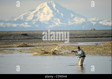 Woman fly fishing for wild Steelhead on Deep Creek with Mt. Redoubt in the background, Kenai Peninsula, Southcentral Alaska Stock Photo