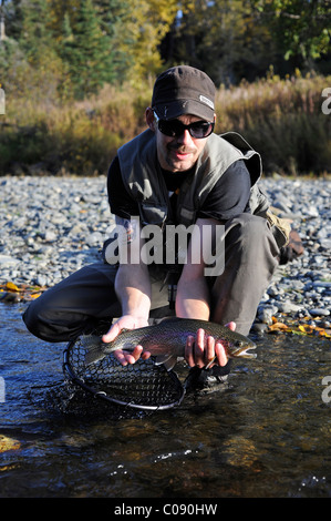 Man kneeling to show off a Rainbow Trout caught in Deep Creek, Kenai Peninsula, Southcentral Alaska, Autumn Stock Photo