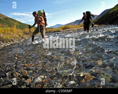 Two female hikers with walking sticks crosses Windy Creek along the Sanctuary River Trail in Denali National Park, Alaska Stock Photo