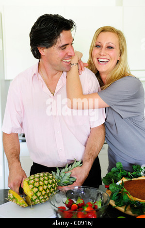 Man cutting a pineapple, young woman leaning on his shoulder Stock Photo