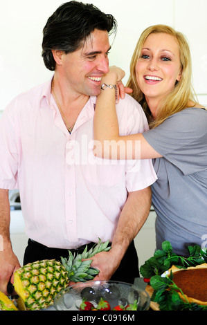 Man cutting a pineapple, young woman leaning on his shoulder Stock Photo