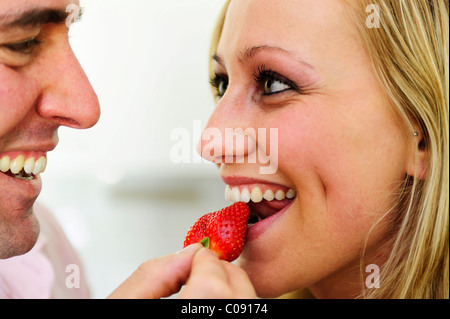 Man holding a strawberry up for a woman to bite into Stock Photo