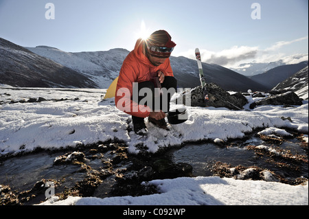 Backpacker fills pan with water from a creek at an alpine camp below Mt. Chamberlin, Brooks Range, ANWR, Arctic Alaska, Summer Stock Photo