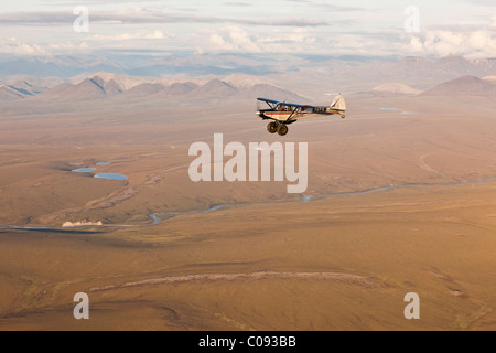 Aerial view of a Piper Super Cub airplane flying over the Jago River with the Romanzof Mountains in the background, ANWR Alaska Stock Photo