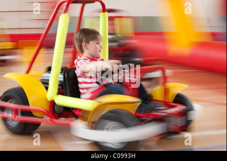 A motion blurred image small boy driving a powered kiddie Kart around an inflatable supervised track Stock Photo