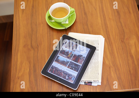 IPad tablet computer with a teacup and a newspaper on a wooden table Stock Photo