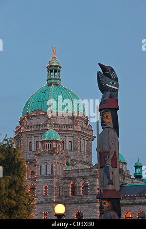 First Nations totem pole in front of the illuminated BC Parliament buildings in the Inner Harbour in the city of Victoria, Vanco Stock Photo