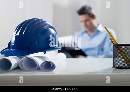 adult caucasian male architect examining documents. Focus on blueprints and hardhat in foreground. Horizontal shape, front view Stock Photo