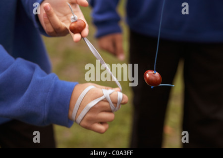 Children playing a game of conkers in the playground at school wearing blue school uniforms Stock Photo
