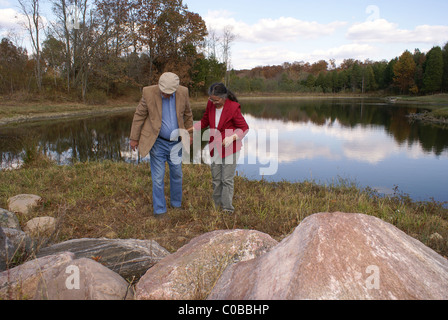 Watching their step, an elderly couple walks away from a lake. Stock Photo