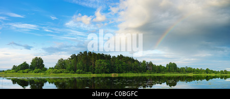 Rainbow over small mountain on the lake coast with smooth water Stock Photo
