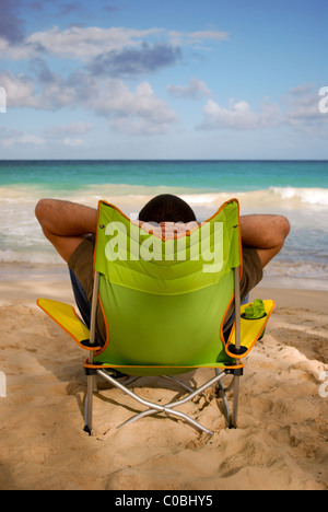 Man in chair relaxing on beach. Person sitting in green collapsible chair. Stock Photo