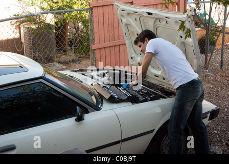 Car Trouble. Man working on car in back yard. Do it yourself mechanic performing auto repair. Examining engine compartment. Stock Photo
