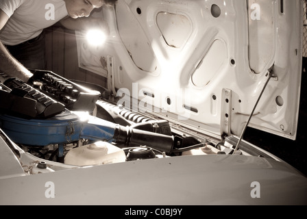 Man working on car by flashlight. Mechanic fixing auto, repair at night. Stock Photo