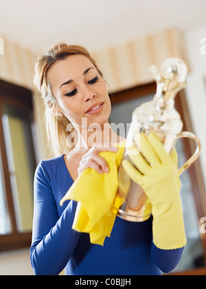 portrait of woman with yellow gloves rubbing silver object. Vertical format Stock Photo
