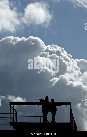 Silhouettes of a man pointing something out to a child before a cloudy sky Stock Photo