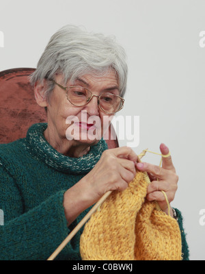 Portrait of an old woman knitting,against a gray background. Stock Photo