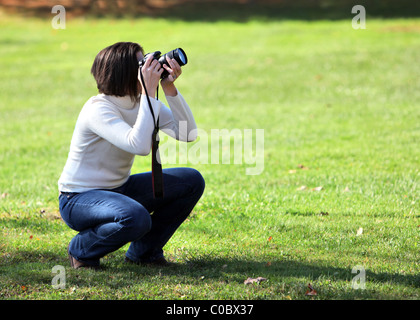 Pretty woman crouching with camera outdoors Stock Photo