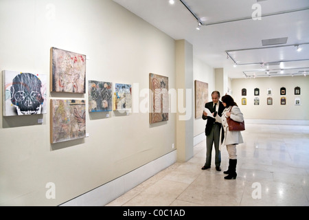 well dressed couple viewing an exhibit of paintings in well lit upscale gallery in Roma district of Mexico City Mexico Stock Photo