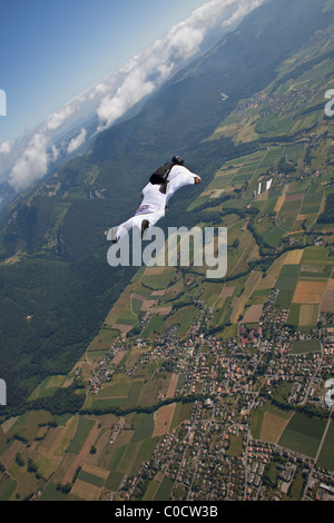 Skydiver within special wingsuit is flying over the edge of clouds and following the green fields in the sky. Stock Photo