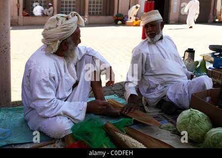 Omani men sit in the shade and sell fruit and vegetables by the souk in Nizwa, Oman. Stock Photo