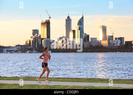 Young woman jogging on path beside river with city in the background. Stock Photo