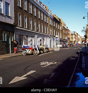 A woman on her mobile phone walking past motorcycles parked on Bermondsey Street, South London SE1 England UK Stock Photo