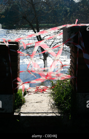 footpath to flooded river blocked with plastic red white tape Stock Photo