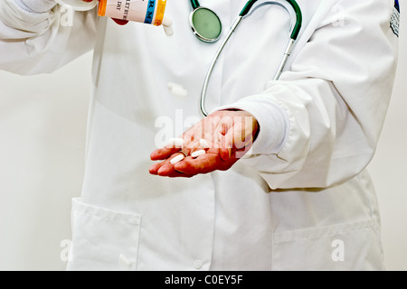 A woman in a doctors smock holding pills in her hand, pouring from a prescription bottle in the other hand, with a stethoscope Stock Photo