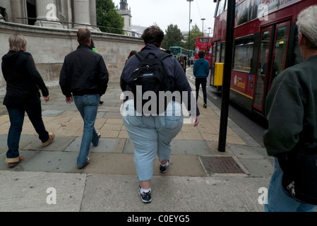 Rear view of an obese woman fat tourist wearing a backpack walking along a street near St Pauls Cathedral in the City of London England UK KATHY DEWITT Stock Photo