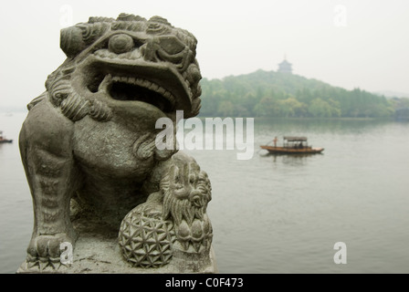 Statue of fu lion beside West Lake, Hang Zhou with Leifeng Tower and boat in the background. Stock Photo